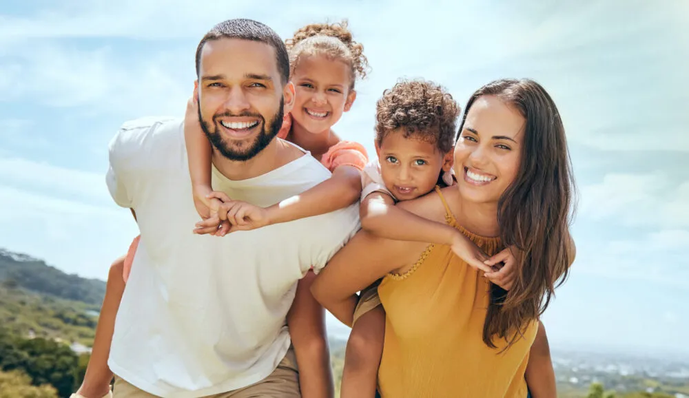 Happy family showing beautiful smiles from orthodontic care Smiling family enjoying time outdoors, representing happy confident smiles from orthodontic care.